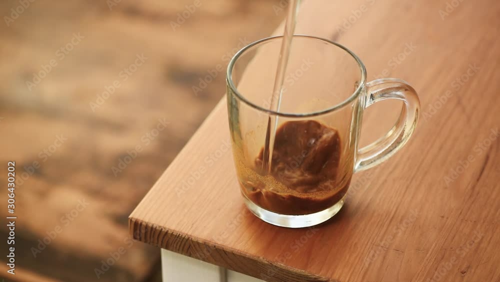 Making instant coffee. Person put teaspoon of instant coffee granules and add hot steaming water in glass cup Making instant coffee. Person put teaspoon of instant coffee granules and add hot steaming water in glass cup