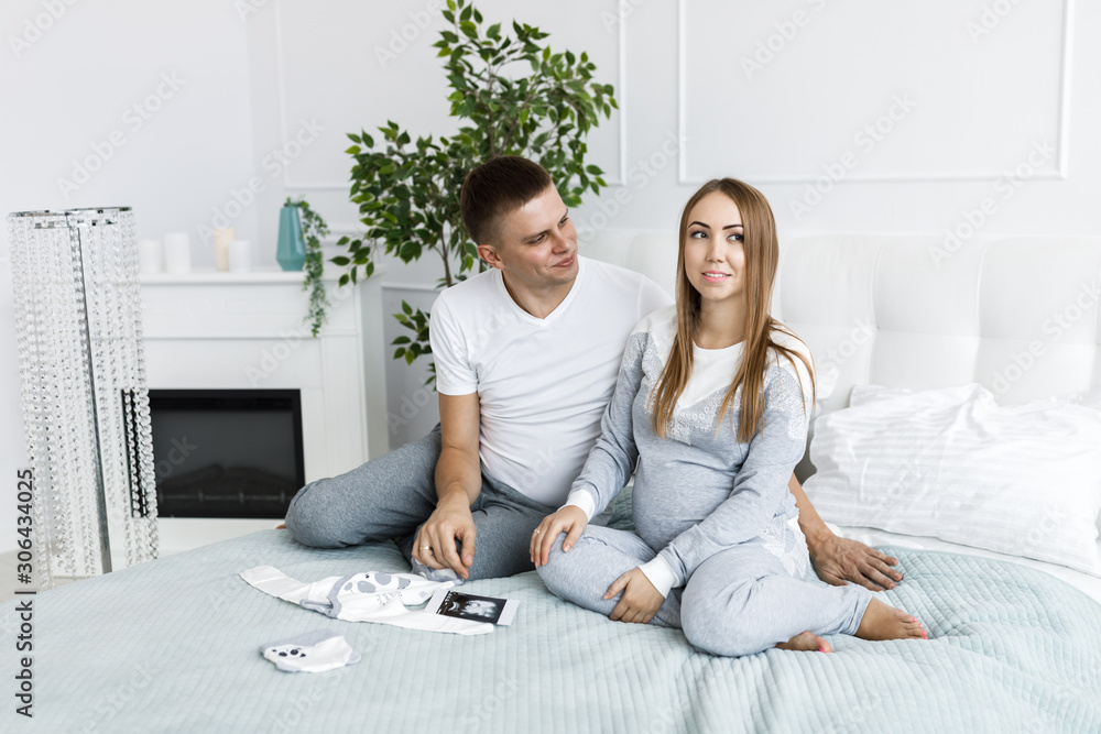 Young couple - man and woman expecting baby, looking at baby clothes and photo. Awaiting the birth of a baby Young couple - man and woman expecting baby, looking at baby clothes and photo. Awaiting the birth of a baby
