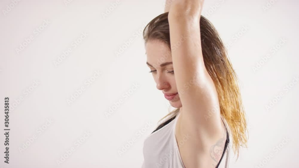 Studio shot of young beautiful woman with tattoos on chest shaking her wet hair and looking at camera with smile while dancing against white background Studio shot of young beautiful woman with tattoos on chest shaking her wet hair and looking at camera with smile while dancing against white background