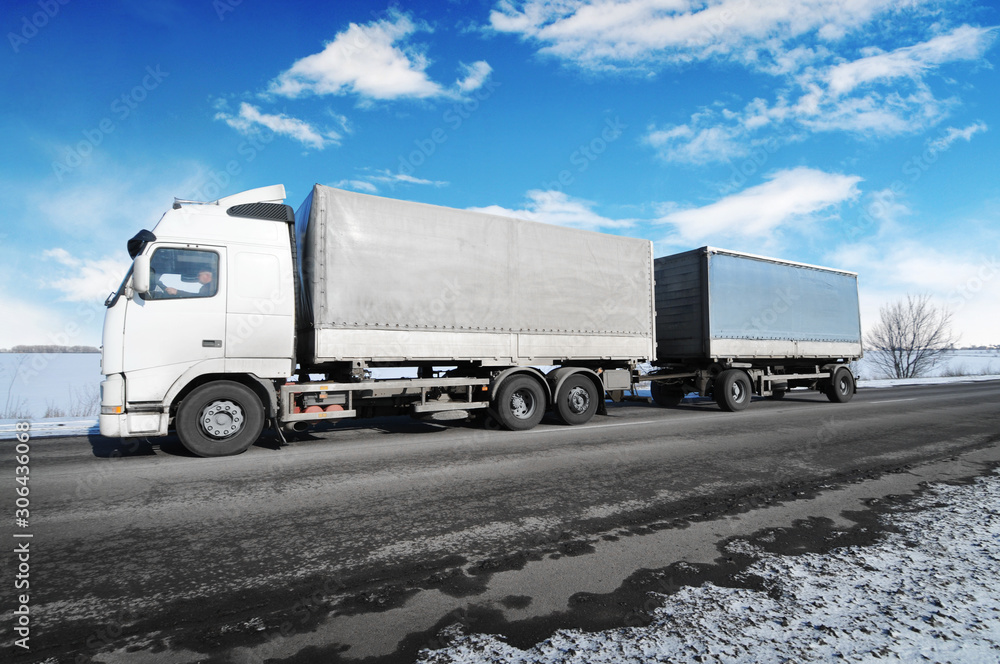 Truck with two trailers on the winter countryside road with snow against sky with clouds Truck with two trailers on the winter countryside road with snow against sky with clouds