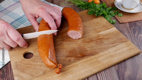 female hands cut smoked sausage on a cutting board on a wooden table photo