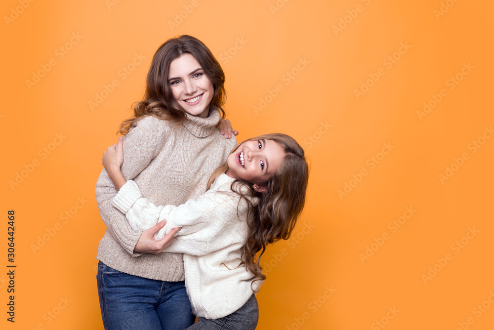 happy family. mother with pretty daughter in a sweater hugging on orange background. happy family. mother with pretty daughter in a sweater hugging on orange background.