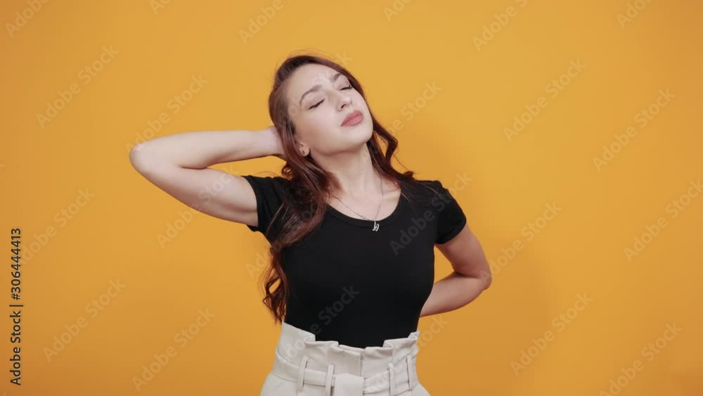 Busy girl in black near yellow background feels very tired of working. She is touching her back as it is because of sitting working a lot she needs some rest. Busy girl in black near yellow background feels very tired of working. She is touching her back as it is because of sitting working a lot she needs some rest.