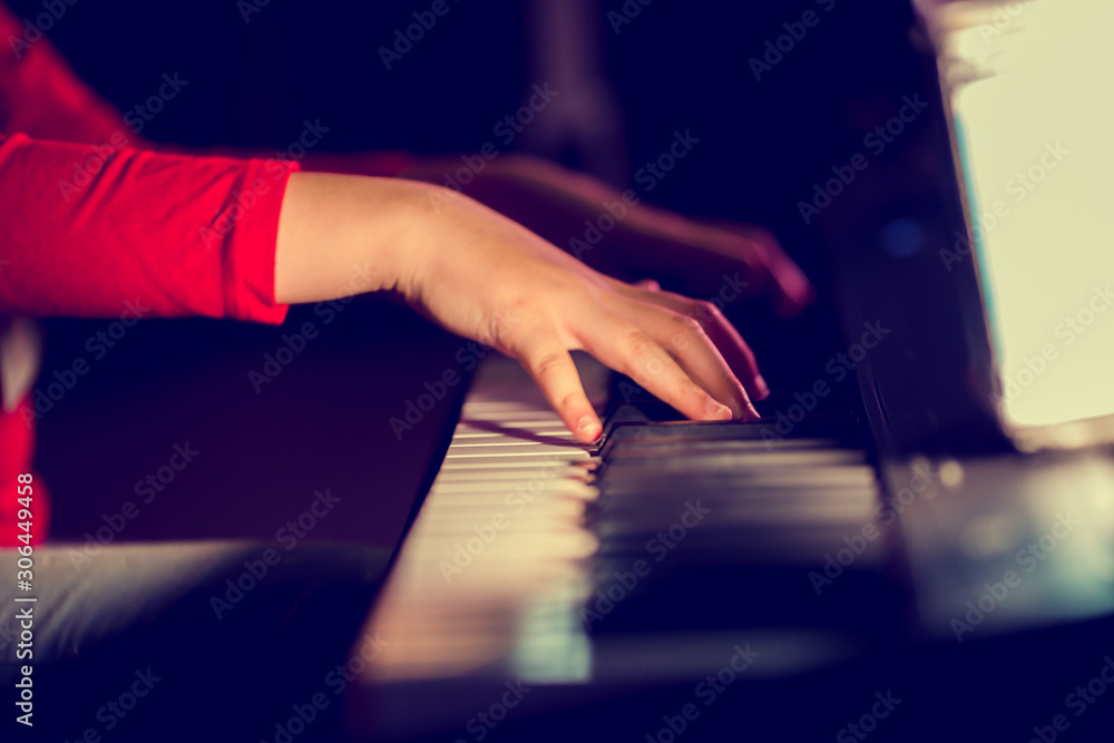 Fototapeta premium Closeup kid's hand playing piano on stage with lighting. Favorite classical music. There are musical instrument for concert or learning music. The concept of musical instrument.