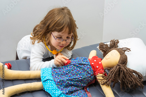 Child girl playing doctor with a soft doll