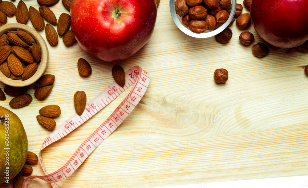 fresh vegetables and fruits with centimeter ribbon, apple, pear, hazelnuts, almonds, glass containers wooden containers on a light wooden background fresh vegetables and fruits with centimeter ribbon, apple, pear, hazelnuts, almonds, glass containers wooden containers on a light wooden background