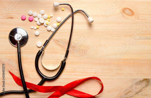 Red ribbon, stethoscope, pills on a wooden table. 1 December World AIDS Day, HIV illness campaign. Copy space for text