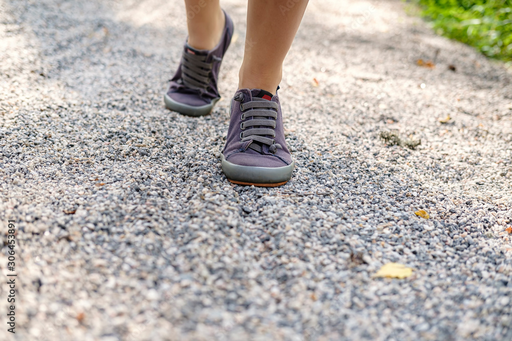 Female legs in sneakers rise up the trail of gravel on a sunny summer day, on a blurred background. Concept of an active lifestyle. Female legs in sneakers rise up the trail of gravel on a sunny summer day, on a blurred background. Concept of an active lifestyle.