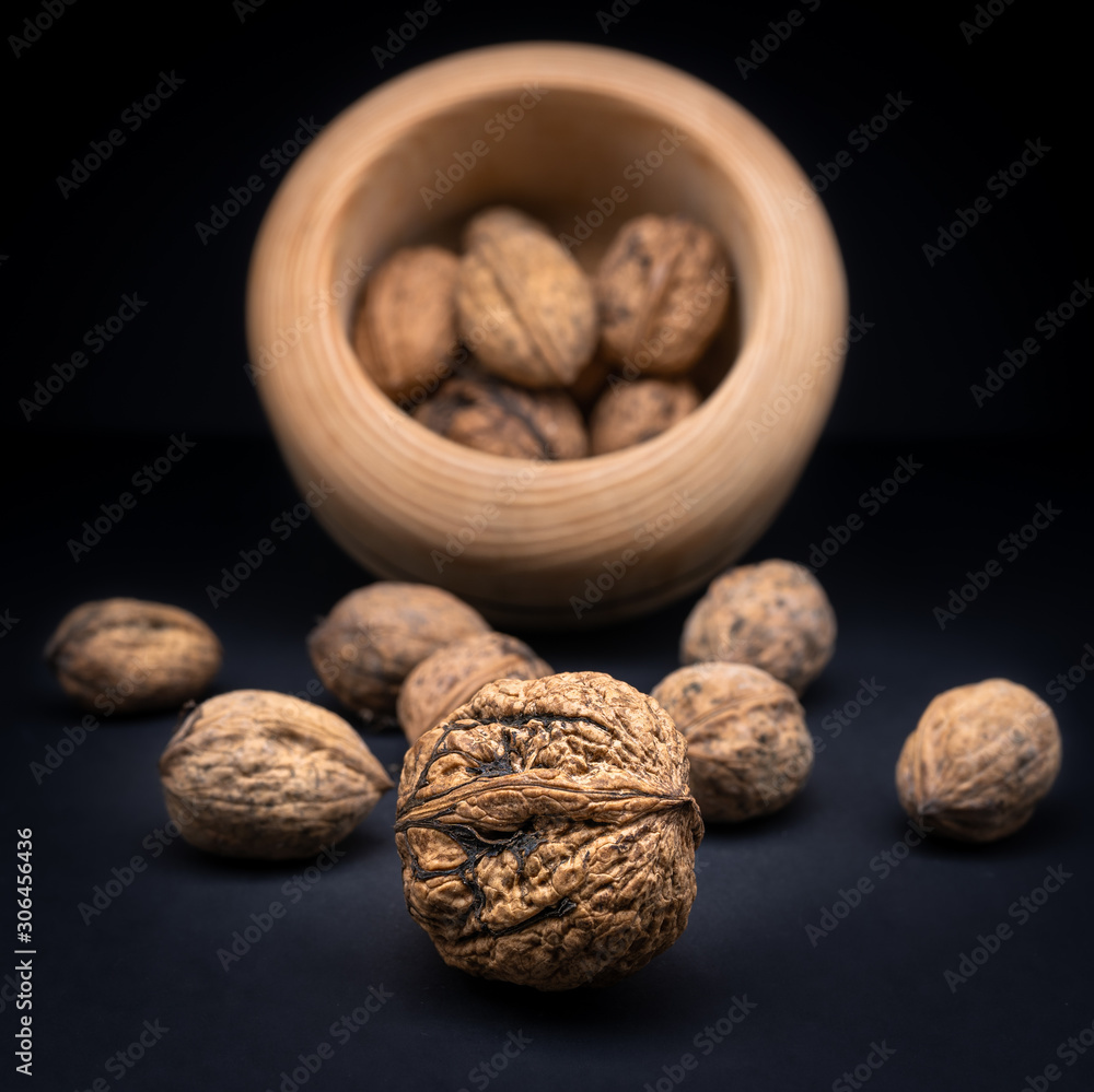 Walnuts in shell in a wooden bowl isolated on black gradient background. Walnuts in shell in a wooden bowl isolated on black gradient background.