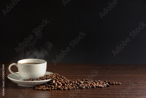 white cup of hot coffee with smoke with coffee beans and on black background