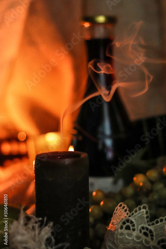 Candle smoke extinct on table with bottle of red wine, grape and soft flamelight on sackcloth background. Soulful autumn photo