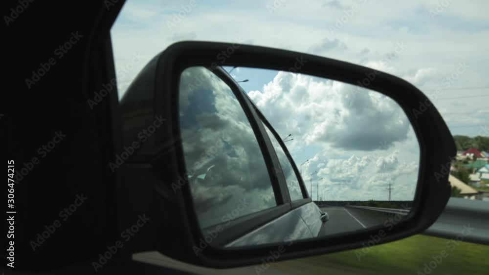 View of side mirror in a car, reflection of clouds and countryroad through the countryside on a summer day View of side mirror in a car, reflection of clouds and countryroad through the countryside on a summer day