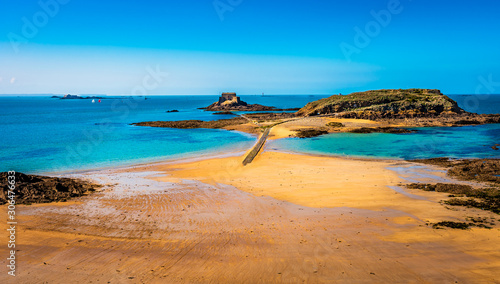 Saint Malo in Brittany, France overlooking the beach and road to the fort islands on a sunny day with green waters and golden sand.