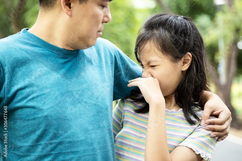 Foul-smelling man was hugging her daughter while her child girl can smell the armpit smelly or the body odor foul from her father with closing her nose,feel stinks,asian male sweat from hot weather