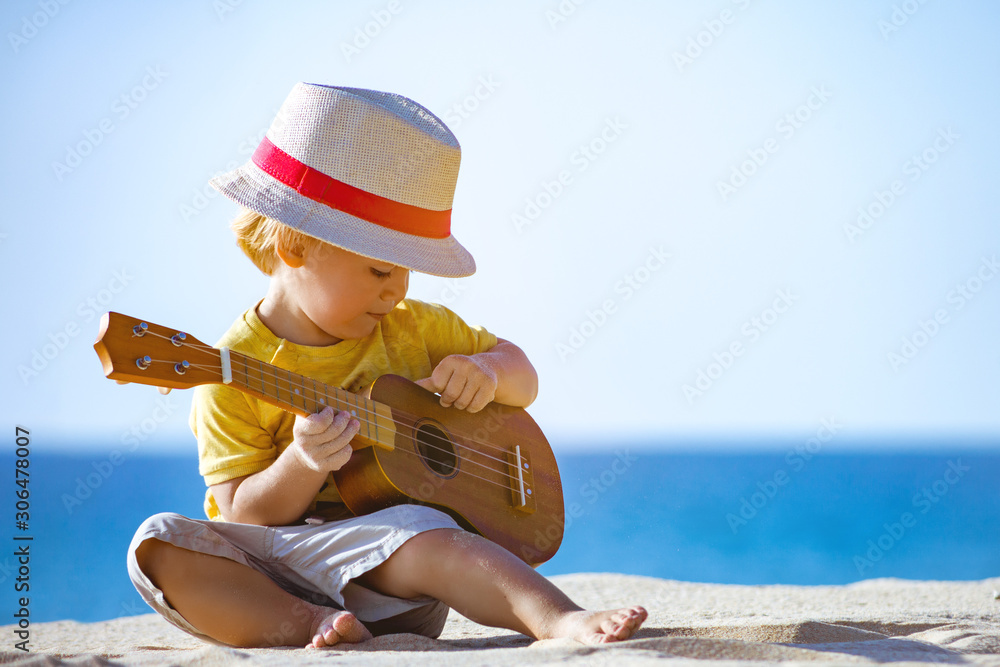 Kid plays on ukulele or small guitar at sea beach - obrazy, fototapety, plakaty 