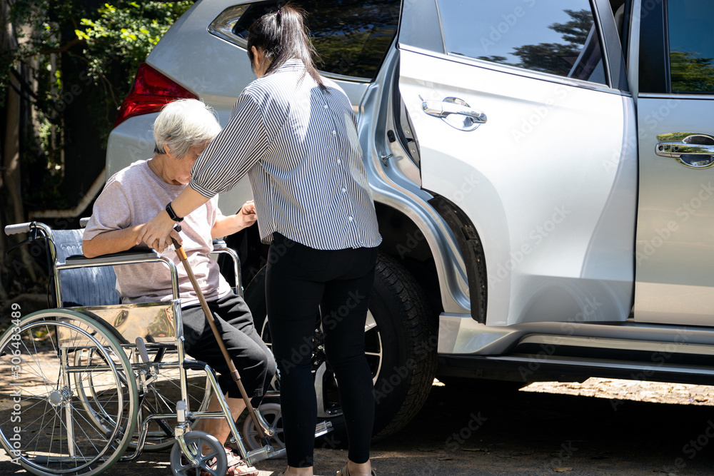 Asian female caregiver helping disabled elderly woman in wheelchair to get into the car,helpful daughter care and support senior mother to stand up from wheelchair in outdoor, caring for old people - obrazy, fototapety, plakaty 
