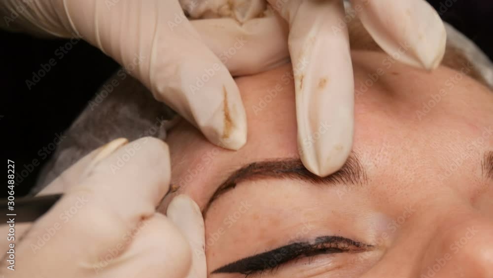 Microblading eyebrow tattoo, permanent makeup. A master in gloves, using special needle, injects pigment into the skin and stains the eyebrows using hair technique, making them natural, close-up view Microblading eyebrow tattoo, permanent makeup. A master in gloves, using special needle, injects pigment into the skin and stains the eyebrows using hair technique, making them natural, close-up view
