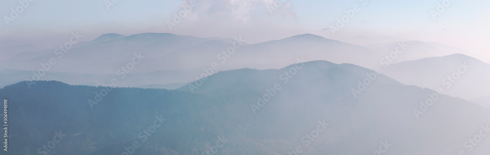 Silhouettes of blue mountain ranges and peaks in the morning fog and haze. Carpathian region. Banner format. Silhouettes of blue mountain ranges and peaks in the morning fog and haze. Carpathian region. Banner format.