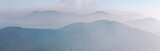 Silhouettes of blue mountain ranges and peaks in the morning fog and haze. Carpathian region. Banner format.