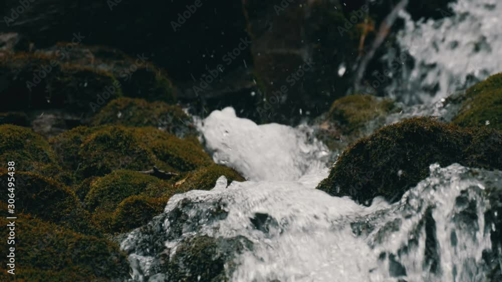 Large old massive black stones covered with green moss on which water flows from a mountain transparent stream Large old massive black stones covered with green moss on which water flows from a mountain transparent stream