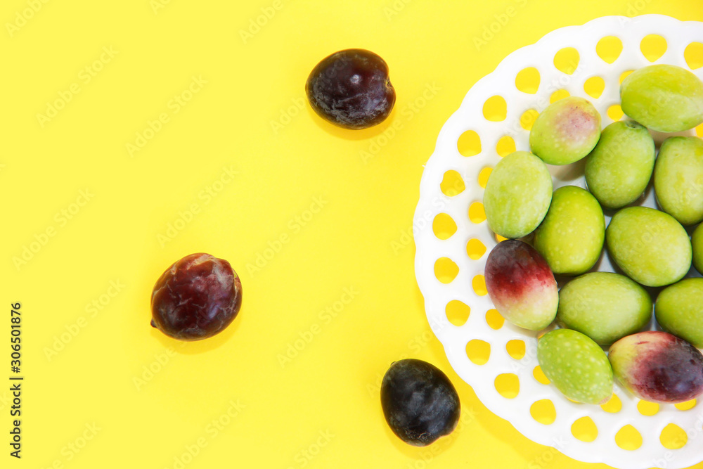 natural round green and brown olives in a decorative plate on a yellow background natural round green and brown olives in a decorative plate on a yellow background