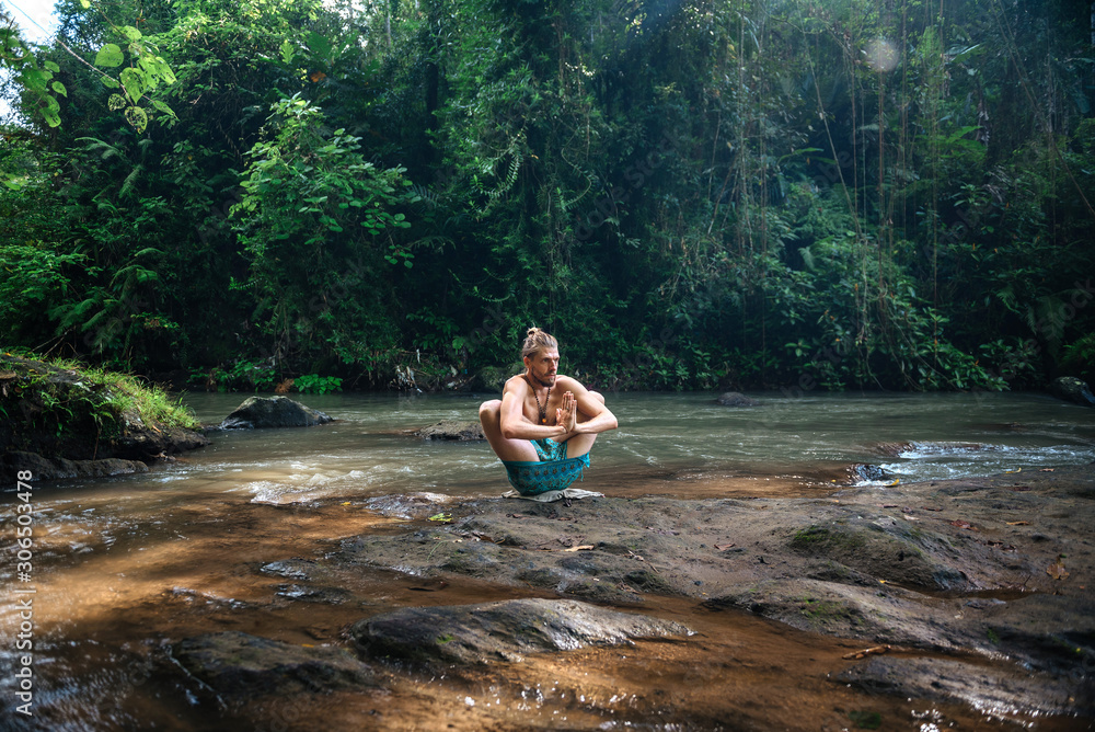 Fototapeta premium Yoga practice and meditation in nature. Man practicing near river