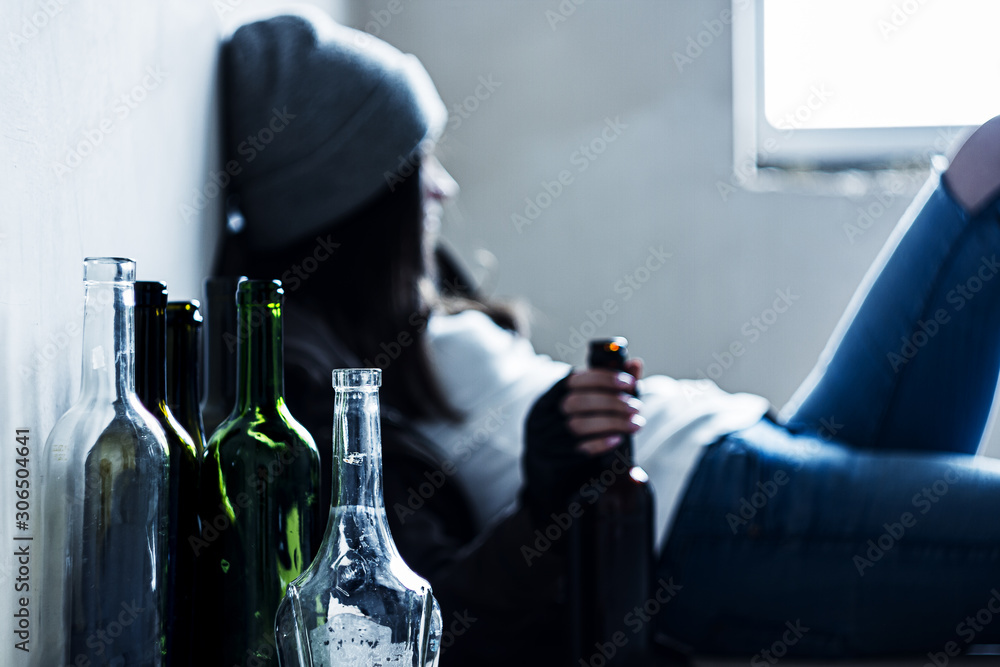 Homeless drunk young woman in hat is sitting on floor in abandoned  building. Addicted teenage girl drunkard is drinking beer. Bum is living in  street. Alcoholism, alcohol abuse concept. Stock Photo |