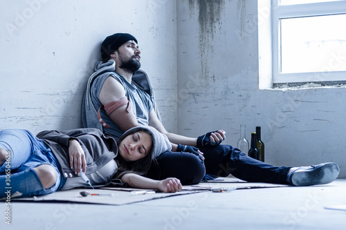 Fotografi Homeless young man and woman are lying on cardboard on floor in abandoned house