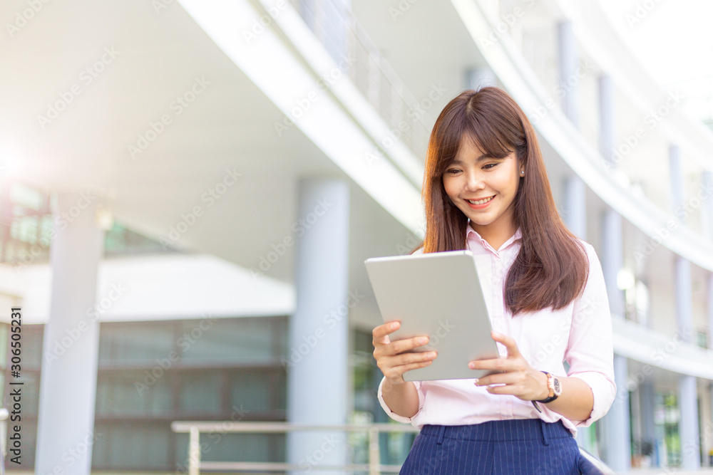 Happy young attractive business woman in her pink shirt using her tablet computer to check her social media outside of her office building Happy young attractive business woman in her pink shirt using her tablet computer to check her social media outside of her office building