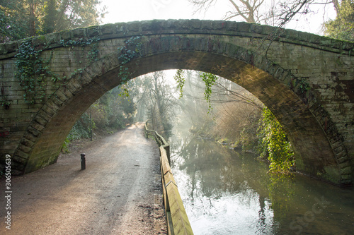 A hump back Victorian bridge is bathed in golden light from an early morning sunrise while the background shows the river's lingering mist picking out the sun's rays