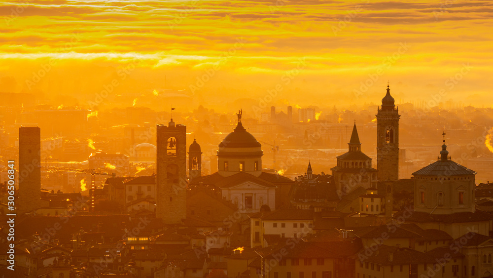 Fototapeta premium Bergamo, one of the most beautiful city in Italy. Amazing landscape at the old town during the sunrise. The fog covers the plain around the town. Fall season. Warm colors contest