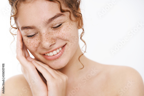 Headshot tender happy smiling naked redhead woman freckles touch perfectly clean pure skin close eyes relieved relaxed laughing joyfully enjoy skin treatment results, look after body white background photo