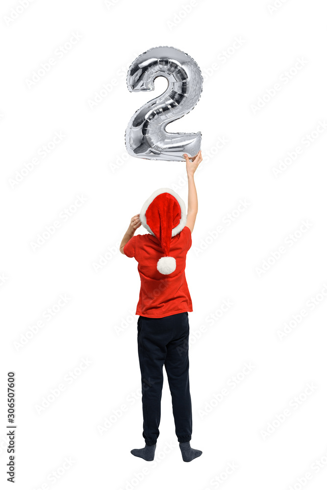 Boy in Santa hat holds up silver inflatable digit two. Back view. Isolated on white background. Boy in Santa hat holds up silver inflatable digit two. Back view. Isolated on white background.