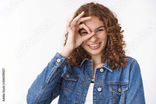 Lucky amused playful cute woman with ginger hair freckles acne prone skin, show okay ok awesome gesture around eye look through happily smiling white teeth, standing joyful white background