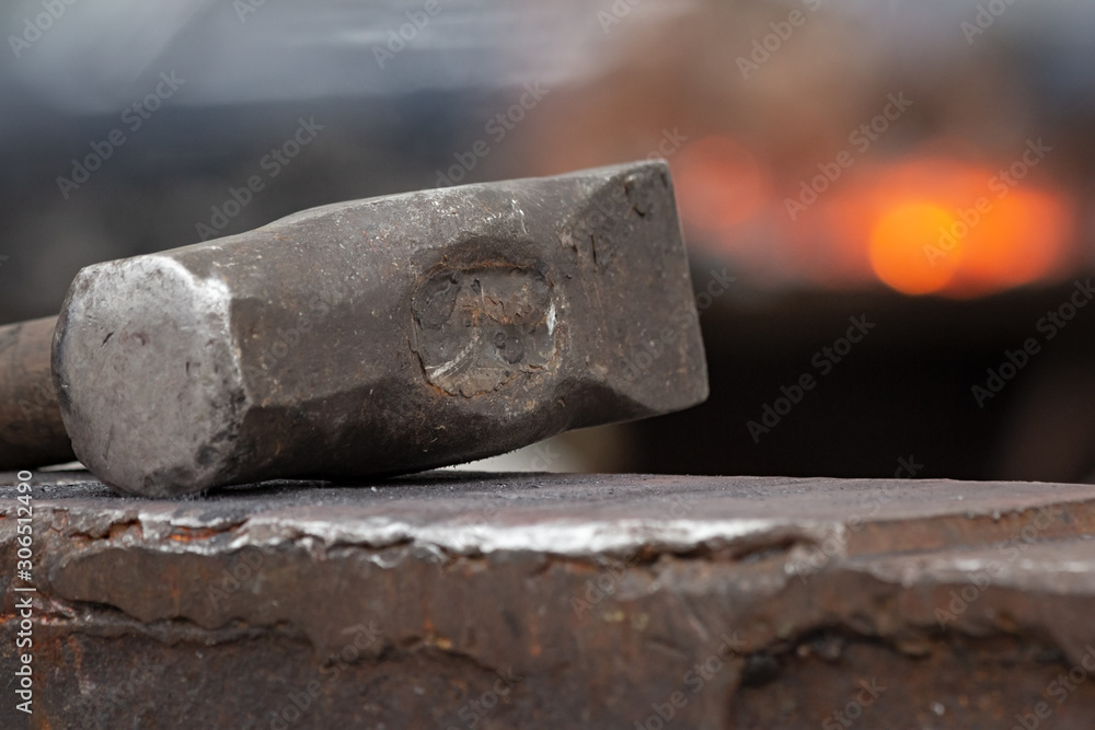 Old rusty hammer lies on the anvil with flame of brazier forge on background. Blacksmith, metalsmith, farrier tools. Close view. Old rusty hammer lies on the anvil with flame of brazier forge on background. Blacksmith, metalsmith, farrier tools. Close view.
