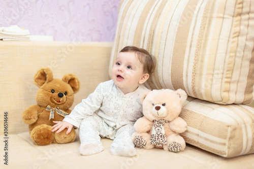 The girl sits on the couch among the toys at home. The concept of family happiness. Photo shoot of the baby for 5-6 months.