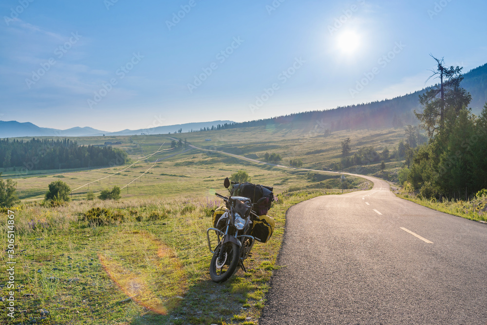 Touring motorcycle parking on asphalt road passing through grassland with sunbeams Touring motorcycle parking on asphalt road passing through grassland with sunbeams