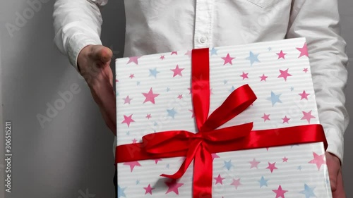 A young man A young man in a white shirt gives a gift a whitein a white shirt gives a gift a white background. Gift box with stars and white ribbon. Concept of holidays. Close up. Man 4k stock footage photo