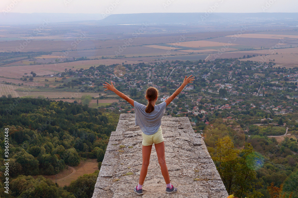 Girl standing at height, arms outstretched to the sky, rear view Girl standing at height, arms outstretched to the sky, rear view