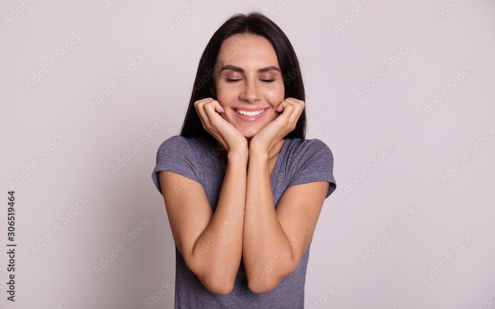 Dreaming of you. Close-up photo of a charming girl with straight jet-black hair, who is smiling broadly with her eyes closed and posing with her hands near her chin.