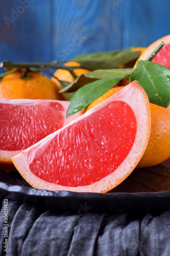 Slices of red grapefruit and whole mandarins with green leaves on the black plate