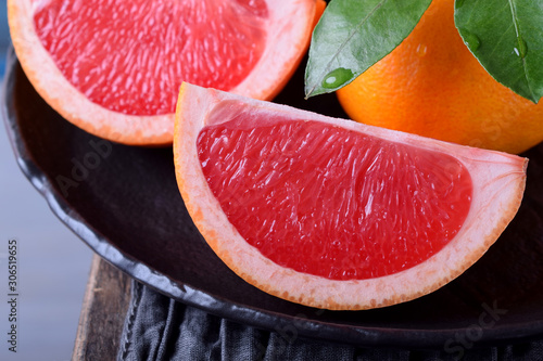 Slices of red grapefruit and whole mandarins with green leaves on the black plate