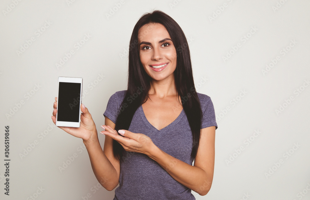 New device. Close-up photo of a wonderful girl with jet-black hair, who is posing with a smartphone in her right hand and pointing at it with her left hand. New device. Close-up photo of a wonderful girl with jet-black hair, who is posing with a smartphone in her right hand and pointing at it with her left hand.