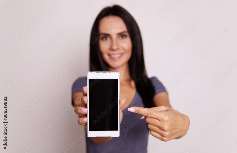 Novelty. Close-up photo of a white smartphone, which is being shown to the camera by a content dark-haired woman in a grey t-shirt. Novelty. Close-up photo of a white smartphone, which is being shown to the camera by a content dark-haired woman in a grey t-shirt.