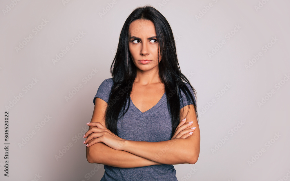 Thinking of injustice. Close-up photo of a young serious woman with long dark hair, who is standing in front of the camera with folded arms and looking aside. Thinking of injustice. Close-up photo of a young serious woman with long dark hair, who is standing in front of the camera with folded arms and looking aside.