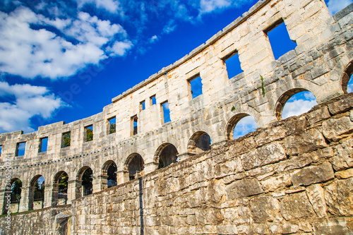 Ancient heritage in Pula, Istria, Croatia. Arches of monumental Roman arena. Detail of historic amphitheater, wide angle view of walls on blue sky background.