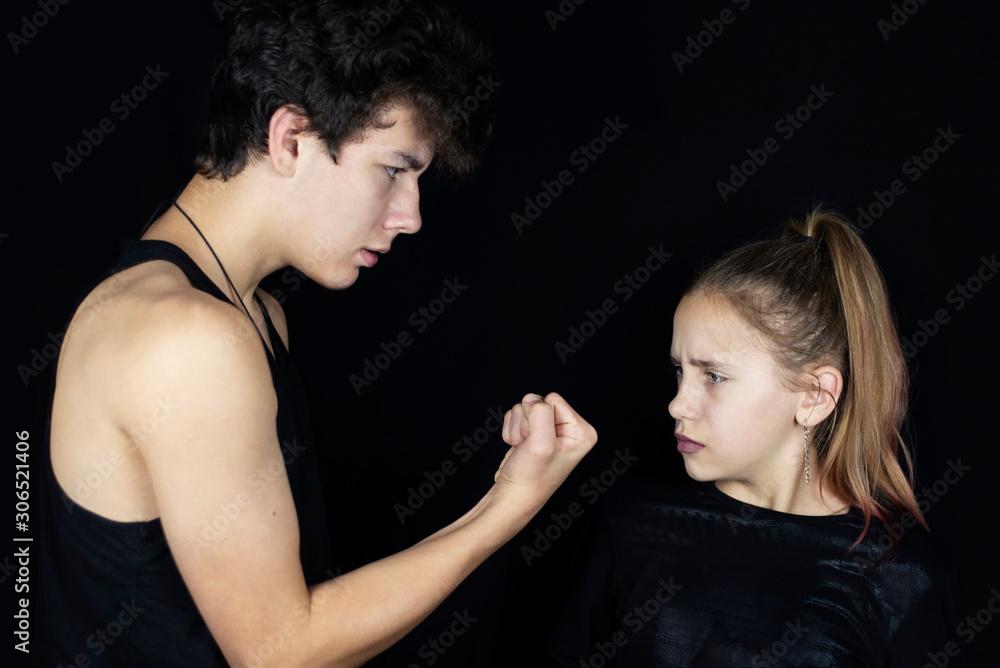 A young girl looks with fear at the guy who threatens her with his fist and humiliates her A young girl looks with fear at the guy who threatens her with his fist and humiliates her