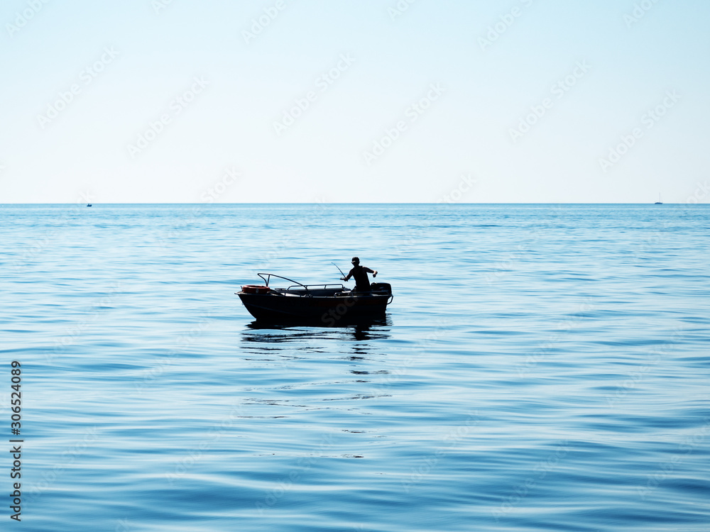 Silhouette of a fisherman in a boat casts a fishing rod into the sea
