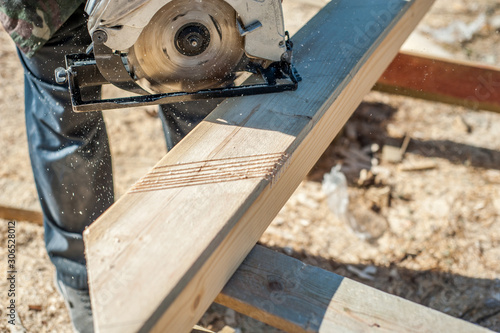 A male carpenter saws with a circular saw a wooden board for the construction of stairs.