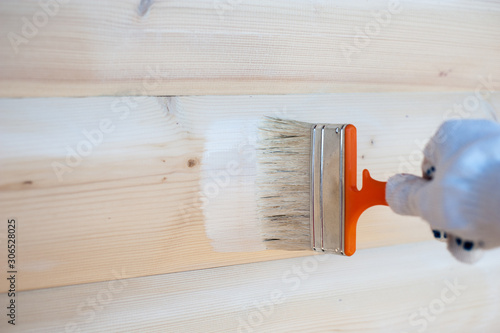 A man paints a wooden house with white paint and a brush on the street.